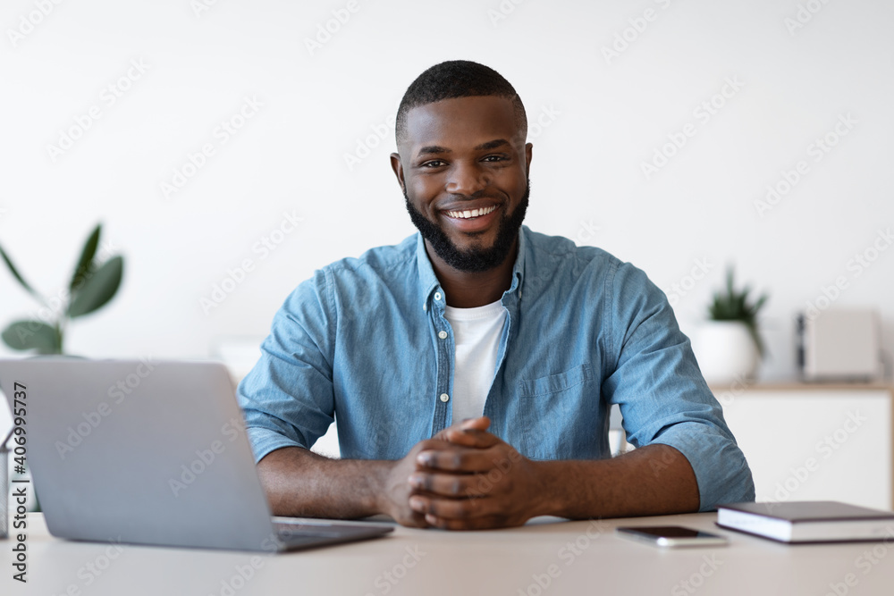 Portrait Of Smiling African Freelancer Man Sitting At Desk In Home Office Portrait Of Smiling African Freelancer Man Sitting At Desk In Home Office
