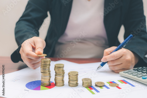 business woman hand putting coin increased coin stacking and use pen point on growth graph and chart with calculator count money saving for financial and accounting concept.
