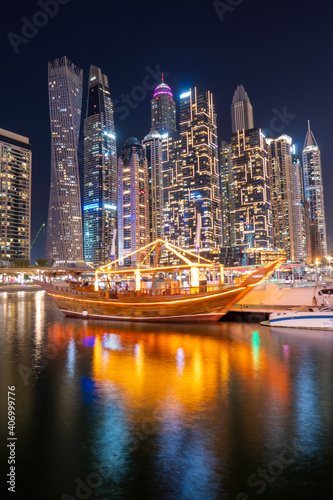 Night view to Dubai Marina panorama, and traditional wooden UAE boat. Luxury skyscrapers represent modern Dubai. Amazing colors reflect on the water. Shot at blue hour. photo