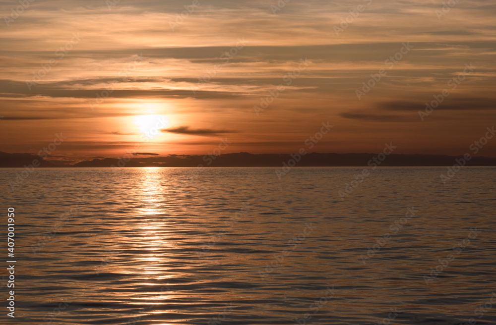 A beautiful, colorful suset over a calm ocean with mountains on the horizon.
