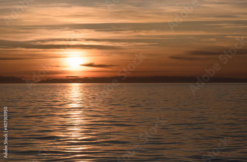 A beautiful  colorful suset over a calm ocean with mountains on the horizon.