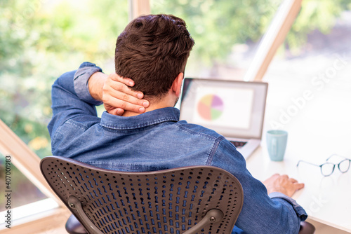 Unrecognizable businessman sitting at office desk and has a pain in his nape