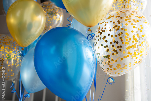 Blue and transparent balloons with golden confetti on the background of a large window. Light interior
