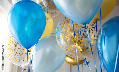 Blue and transparent balloons with golden confetti on the background of a large window. Light interior
