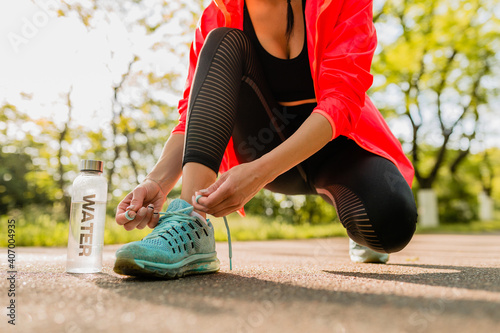 close-up feet of young attractive slim woman lacing shoelaces of sneakers doing sport exercises in morning sunrise jogging in park in sports wear, healthy lifestyle, water bottle