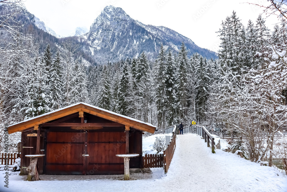 Wooden hut in the Bavarian alps on a cold winter day in January. Snow is covering the trees, mountains and walkways.