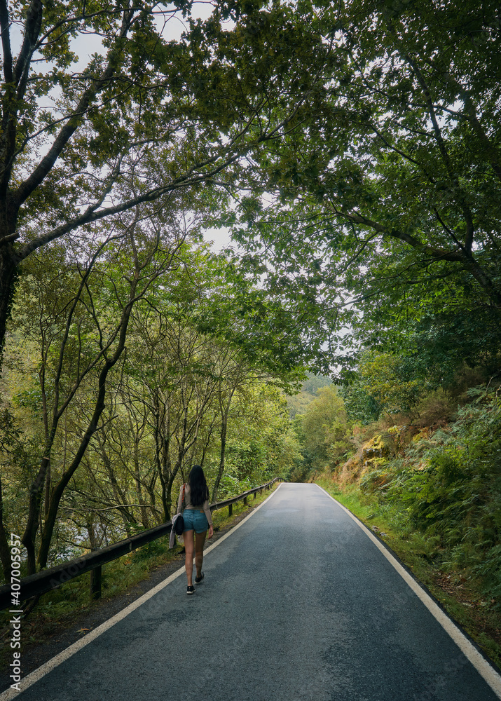 Young woman walking on a road surrounded by forest in summer. Galicia in summer. Santiago's road