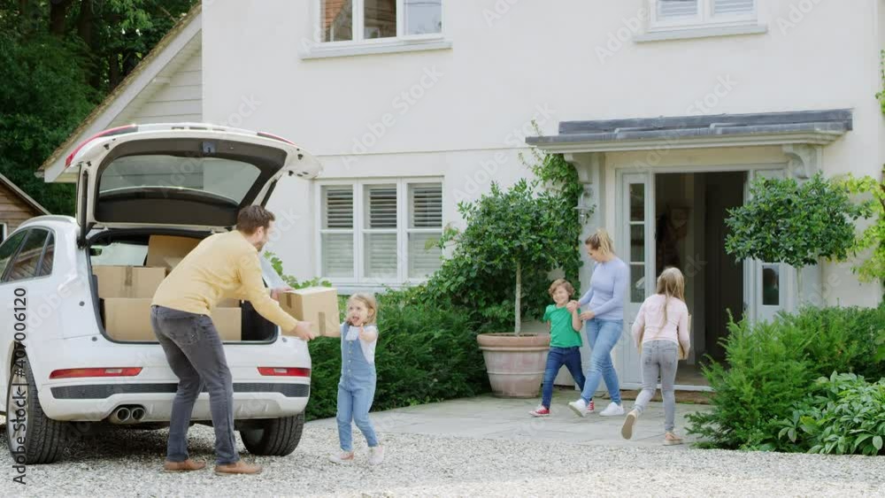 Family unloading boxes from car as they move into new home - shot in slow motion