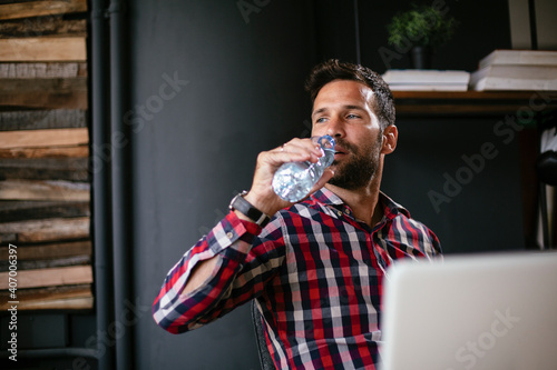 Young businessman using laptop in his office. Thirsty businessman drinking water. Healthy lifestyle