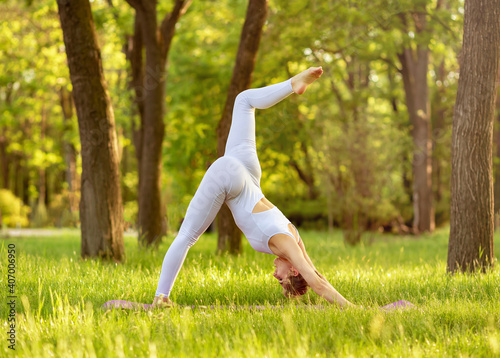 Beautiful woman practicing yoga in morning light. Relax in nature in the park. Healthy life concept. Yoga poses. Female doing yoga on green grass in summer on nature. Young woman enjoying meditation.