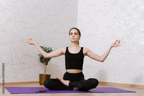 Tranquil woman in activewear sitting on mat in Lotus pose with crossed legs and mudra gesture while practicing yoga at home and looking away 