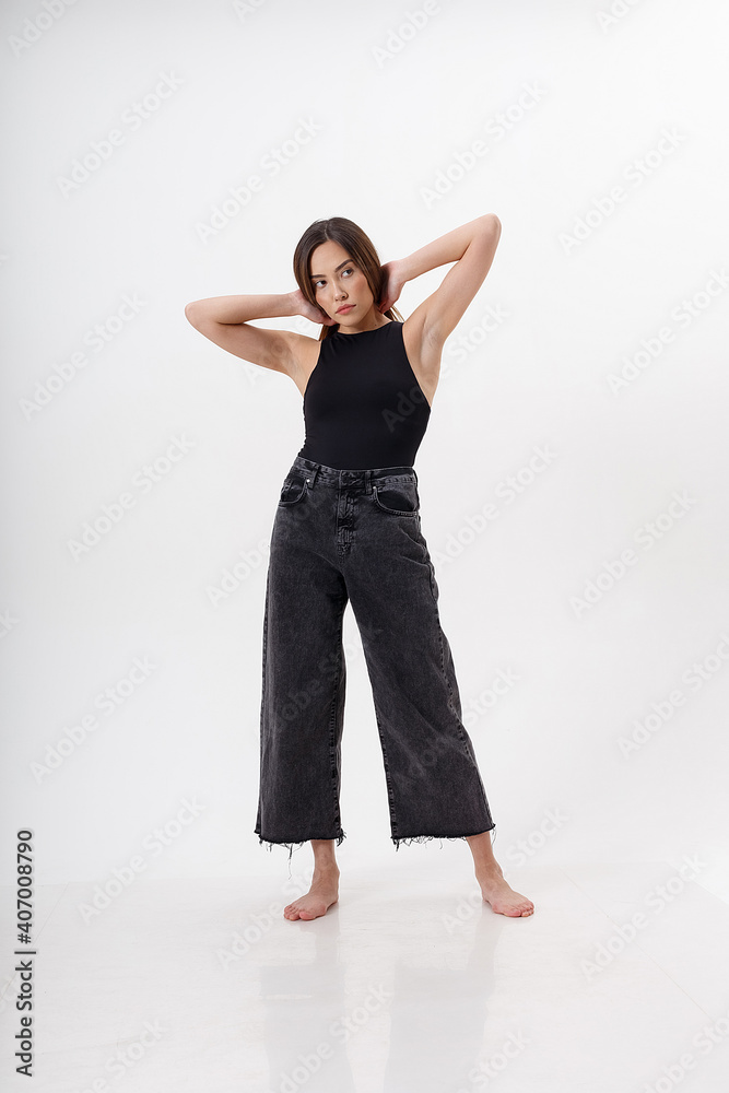 portrait of young attractive asian woman with long hair in black bodysuit, jeans, isolated on white studio background. skinny pretty female posing on cyclorama. model tests of beautiful lady