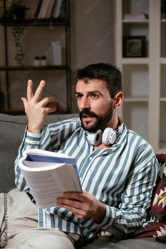 Fototapeta premium Man at home studying. Young man reading a book on the couch.