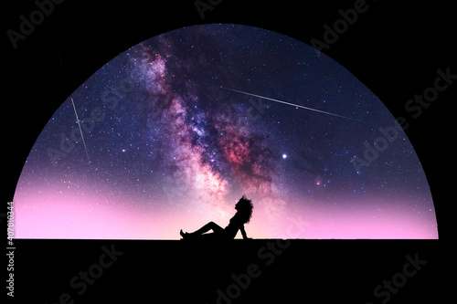 Silhouette of a girl sitting near the arch, behind her beautiful starry sky with milky way galaxy. Night photography.