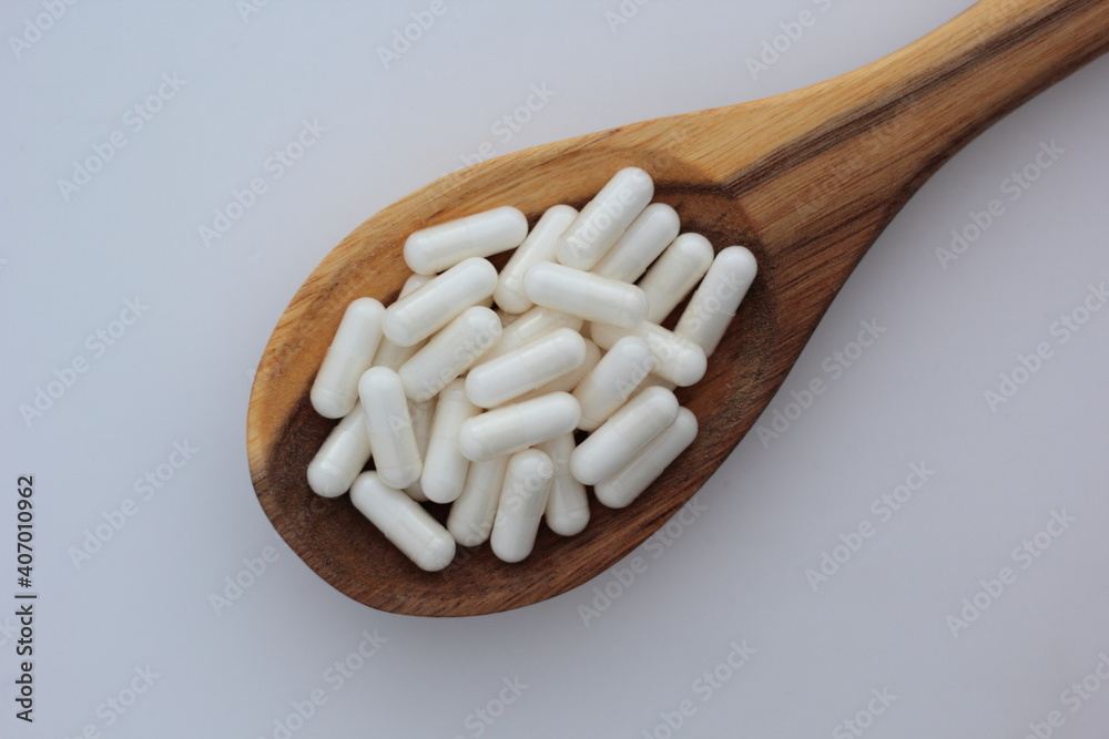 Closeup of myo-inositol capsules on a wooden spoon. Myo-inositol is a commonly used supplement for treating PCOS symptoms.