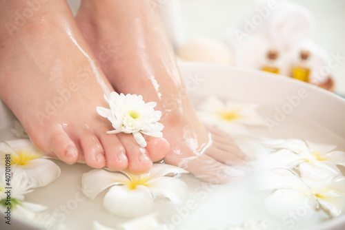 closeup view of woman soaking her feet in dish with water and flowers on wooden floor. Spa treatment and product for female feet and hand spa. white flowers in ceramic bowl.