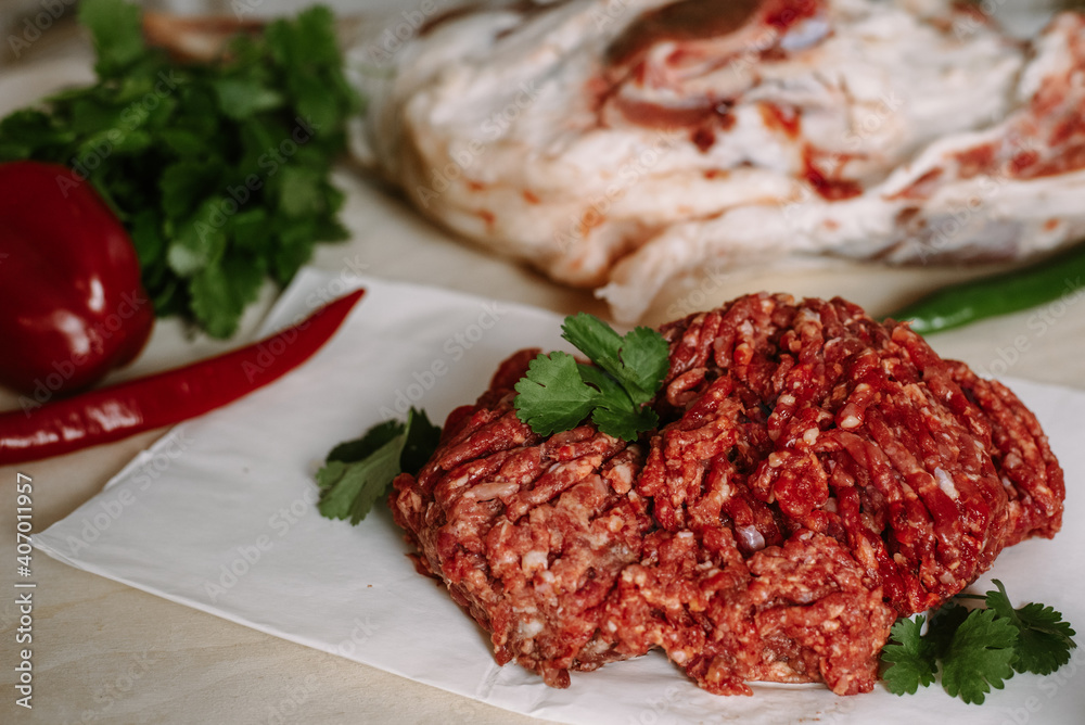 Red fresh minced meat on the background of lamb legs, red pepper and greens Red fresh minced meat on the background of lamb legs, red pepper and greens