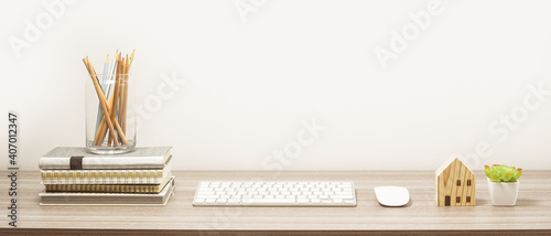 Workspace with book, keyboard and home model on wood table with living room white wall. Panoramic banner of workplace with copy space