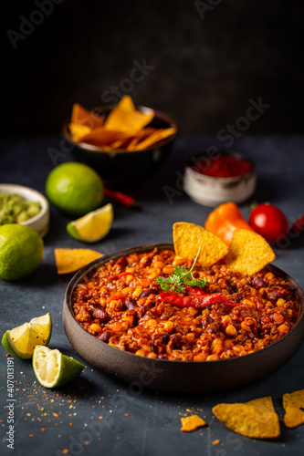 Mexican hot chili con carne in a bowl with tortilla chips on dark background
