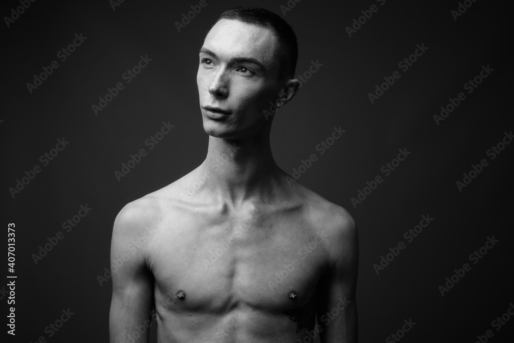 Young handsome androgynous man shirtless against gray background