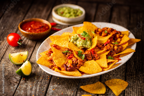 Delicious plate of yellow corn nachos chips with cheese, minced meat and red hot spicy salsa over wooden table