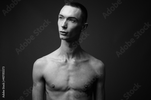 Young handsome androgynous man shirtless against gray background