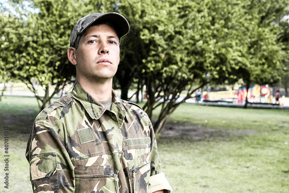 Portrait of guard in park. Serious man in military camouflage uniform standing in park, looking at camera. Medium shot. Military man or guard concept