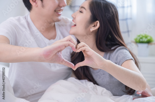 Close up hand of young Asian couple doing heart gesture together by hands and smiling or laughing together on white bed in bed room.