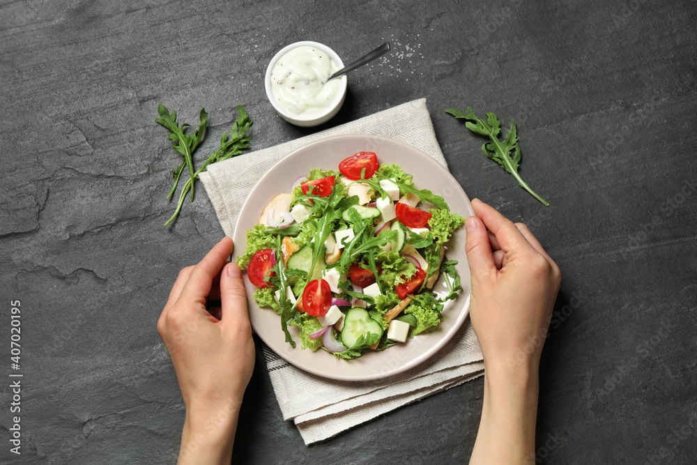 Woman holding plate with delicious arugula salad at black table, top view