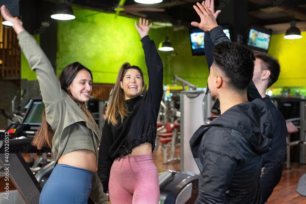 Fototapeta premium Happy diverse group of friends, high five celebrating, enjoying fitness workout together in gym. High quality photo.