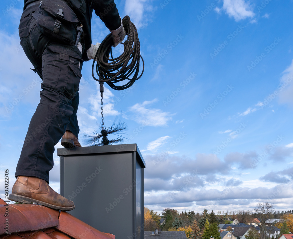 Chimney sweep man in work uniform cleaning chimney on building roof ...