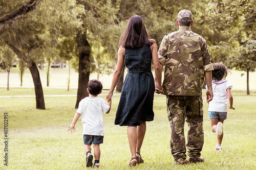Military man walking in park with his wife and children  kids and parents holding hands. Full length  back view. Family reunion or military father concept