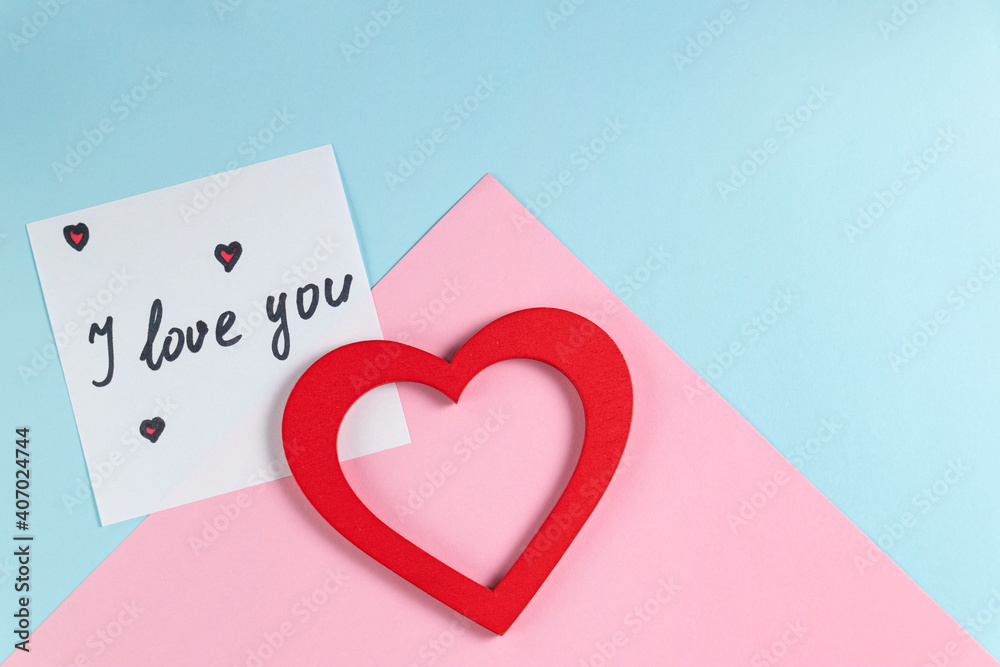 Valentine's Day background. Red heart and note with the words I love you on pastel blue and pink colors. Valentine's Day concept. Flat lay.