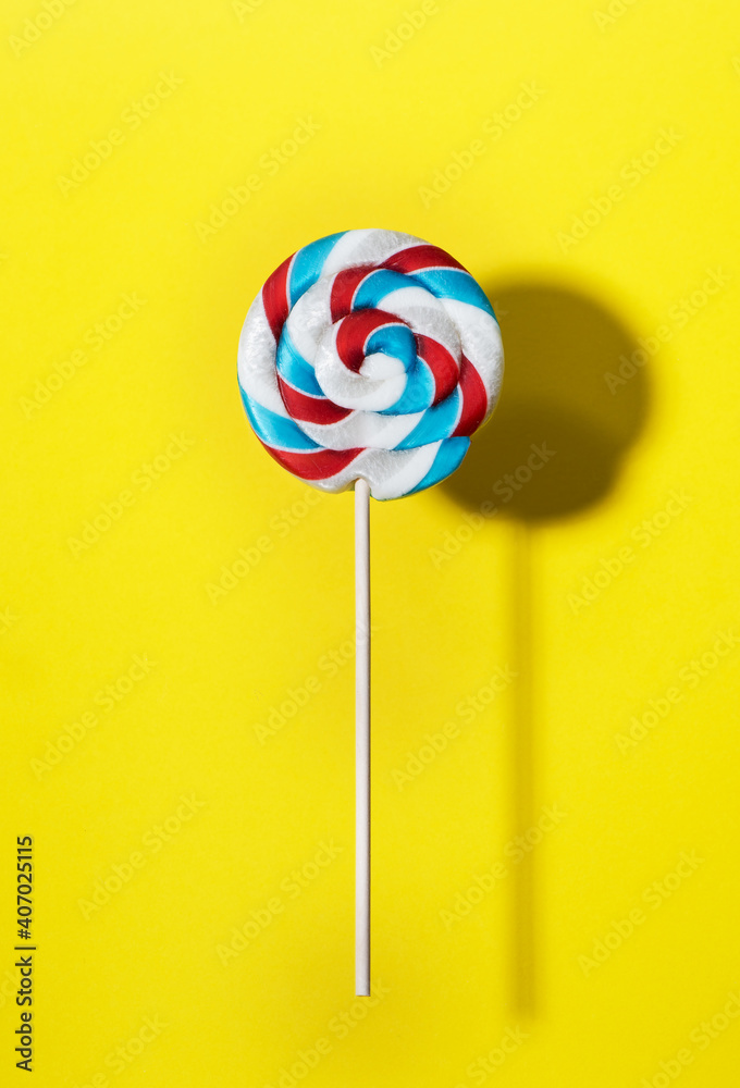 Swirl lollipop candy on a stick on yellow background, top view