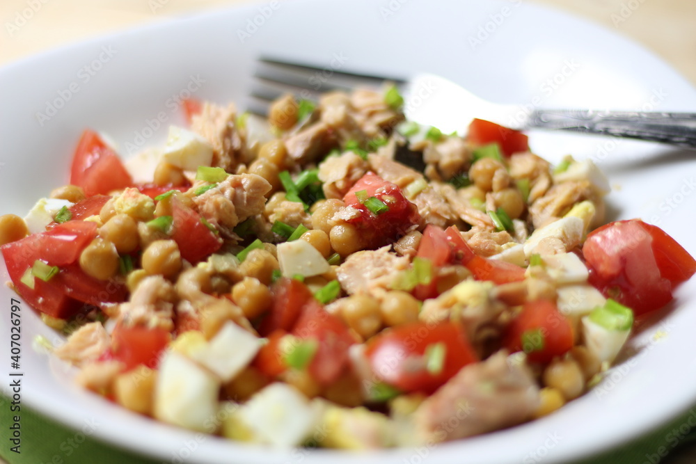 Salad with chickpea, salmon, tomato, egg, green onion, olive oil in white bowl with fork