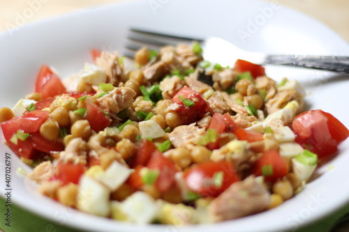 Salad with chickpea, salmon, tomato, egg, green onion, olive oil in white bowl with fork