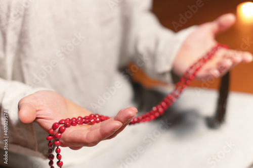 close-up of a male practitioner's hand sitting in lotus position in a dark meditation room with a rosary in his hands
