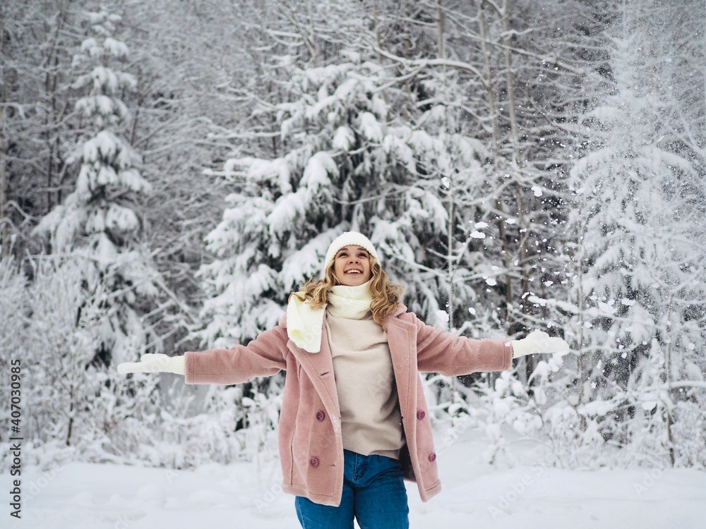 Happy young woman plays with a snow in winter day. Girl enjoying winter, frosty day. Playing with snow on winter holidays, a woman throws white, loose snow into the air. Walk in winter forest