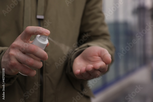 Man spraying antiseptic on his hand outdoors, closeup