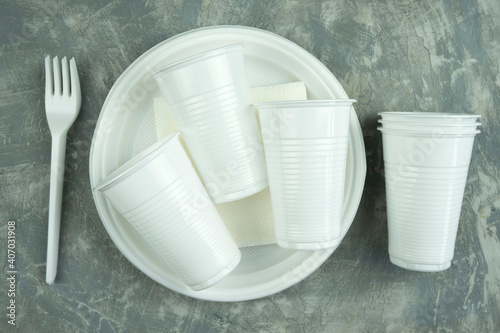 plastic dishes on a concrete background. plastic plates, forks, knives, glasses.
