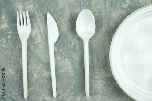 plastic dishes on a concrete background. plastic plates, forks, knives, glasses.