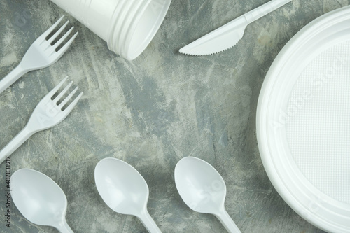 plastic dishes on a concrete background. plastic plates, forks, knives, glasses.