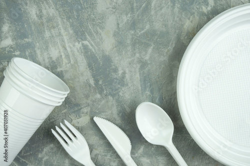 plastic dishes on a concrete background. plastic plates, forks, knives, glasses.