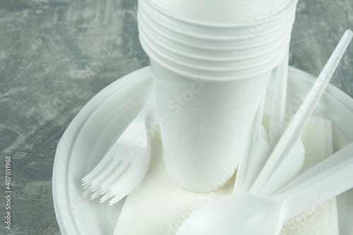 plastic dishes on a concrete background. plastic plates, forks, knives, glasses.