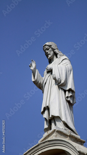 Jesus Christ statue atop a church with blue sky in the background - Savior concept.
