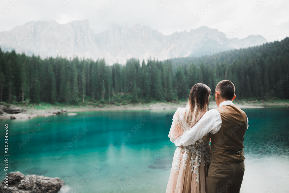 Wedding couple on the nature is hugging each other near a beautiful lake in the mountains.. Beautiful model girl in white dress. Man in suit