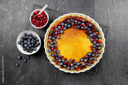 Delicious cheesecake tart with fresh blueberries and cranberries, on a dark stone background. Top view.
