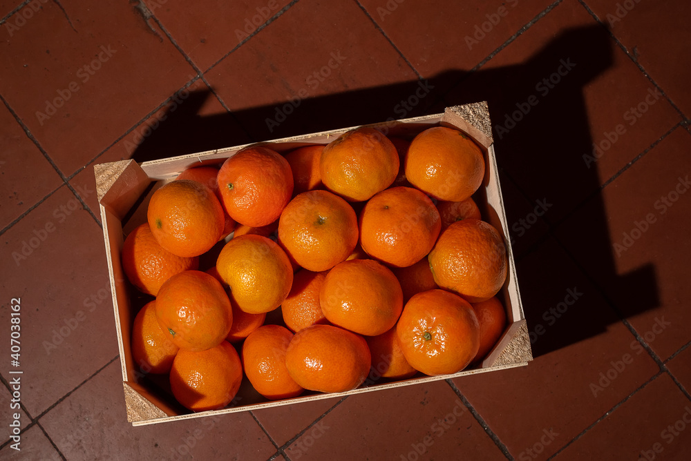 Tangerines (oranges, clementines, citrus) in wooden box on garnet tiles background. Top view.