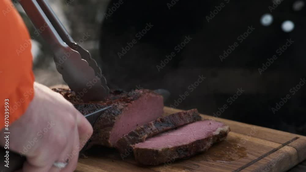 chef cuts pastrami steak on board. freshly cooked steak is removed from grill and cut into small strips to be fried or smoked separately. Winter, outdoor cooking chef cuts pastrami steak on board. freshly cooked steak is removed from grill and cut into small strips to be fried or smoked separately. Winter, outdoor cooking