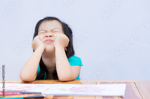 Pupil self isolating herself in doing art homework. Child bored or frustrated and frantic face. Kid pull their faces with both hands. Girl stay at home during covid-19 lockdown. Social Distance.